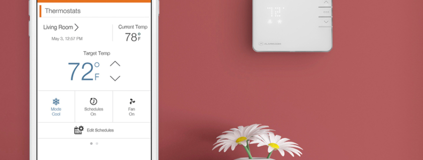 iPhone screen image showing an Alarm.com interface in the foreground and a smart wall thermostat in the background.