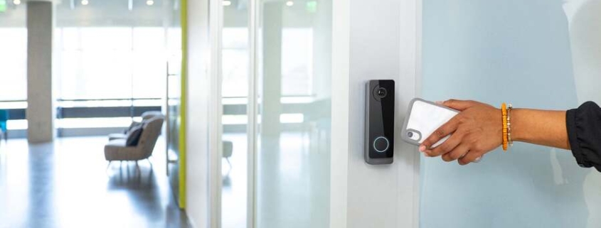 Person holding a smartphone to an access control reader at a door.